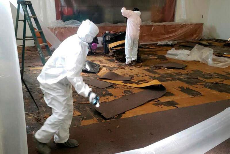 Abatement workers in protective suits removing old floor tiles during asbestos removal